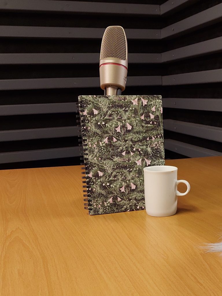 The picture shows a plant-themed notebook leaning on a microphone, and a greyish-white coffee cup.